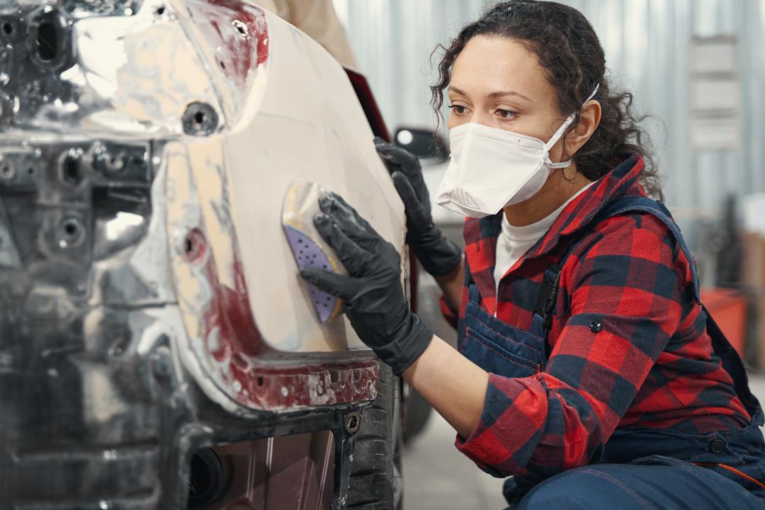 Kobieta szlifuje szpachle na tylnej ćwiartce samochodu ponieważ to dobry blacharz lakiernik Kraków